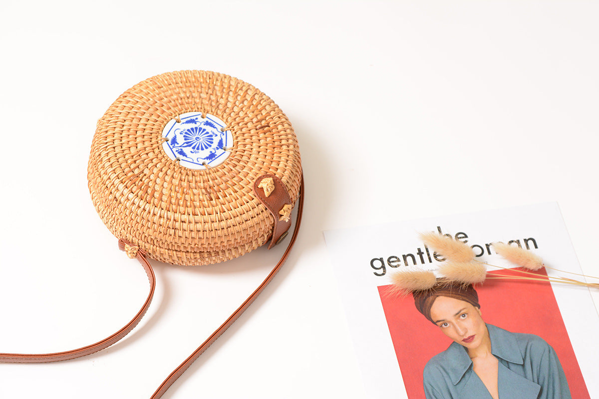 Omi Woven Handbag — Round woven handbag with a blue floral ornament.